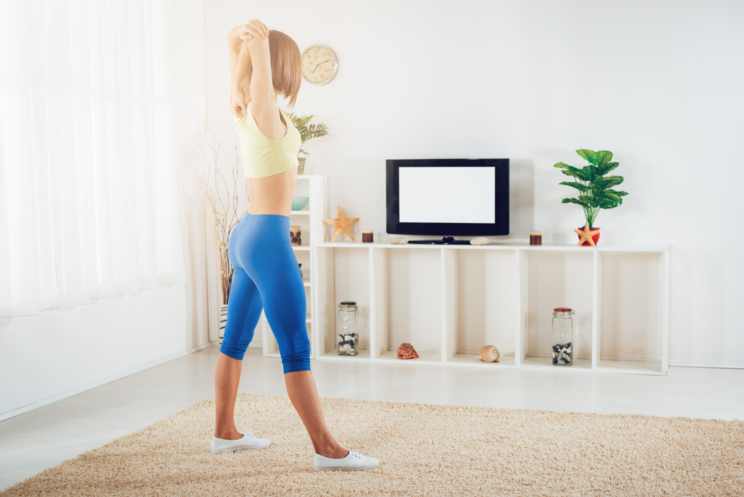 Fit woman warming up while doing stretching exercises at home in front of TV.